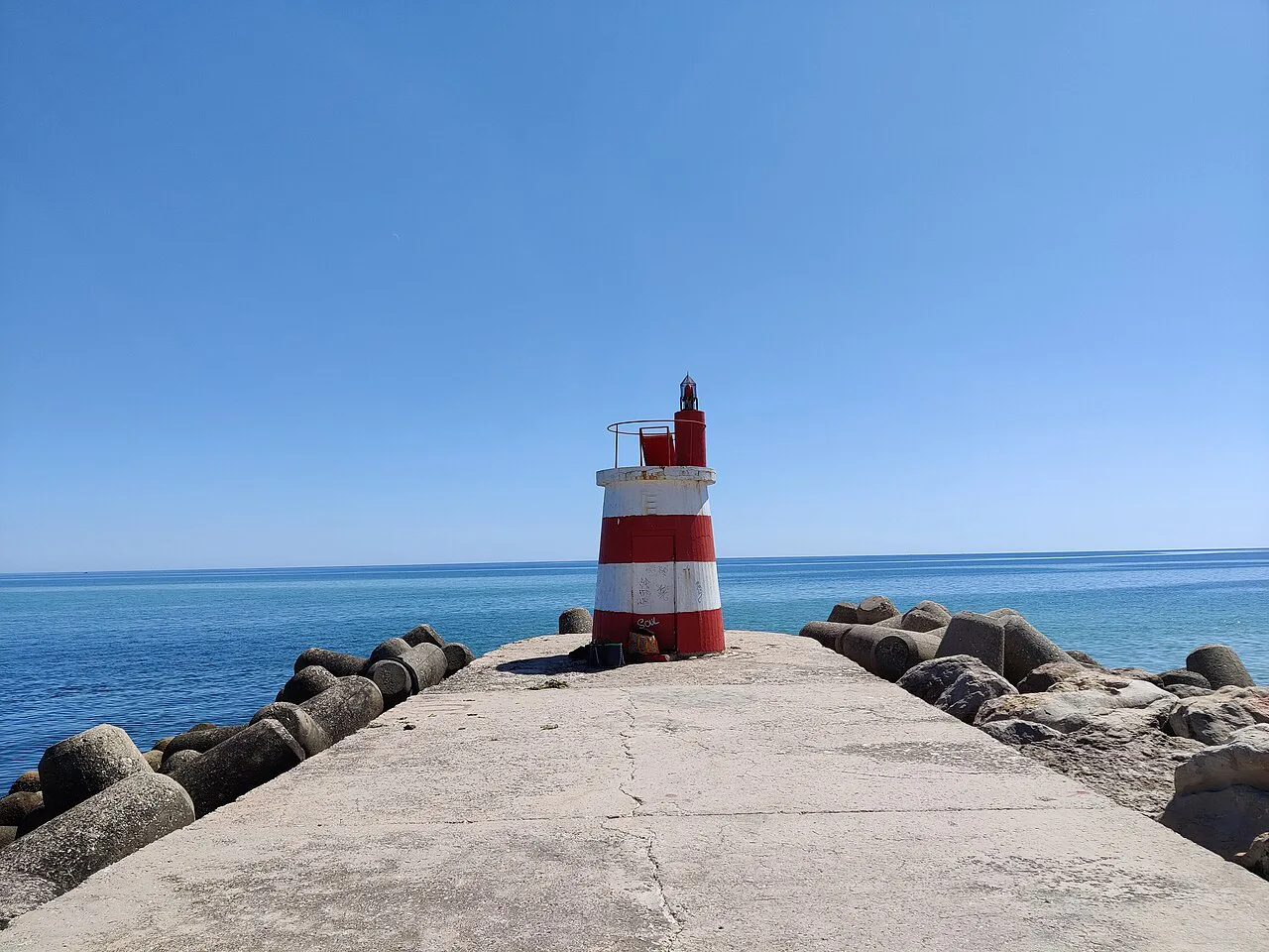 A red-and-white beacon at the end of a breakwater at Tavira.