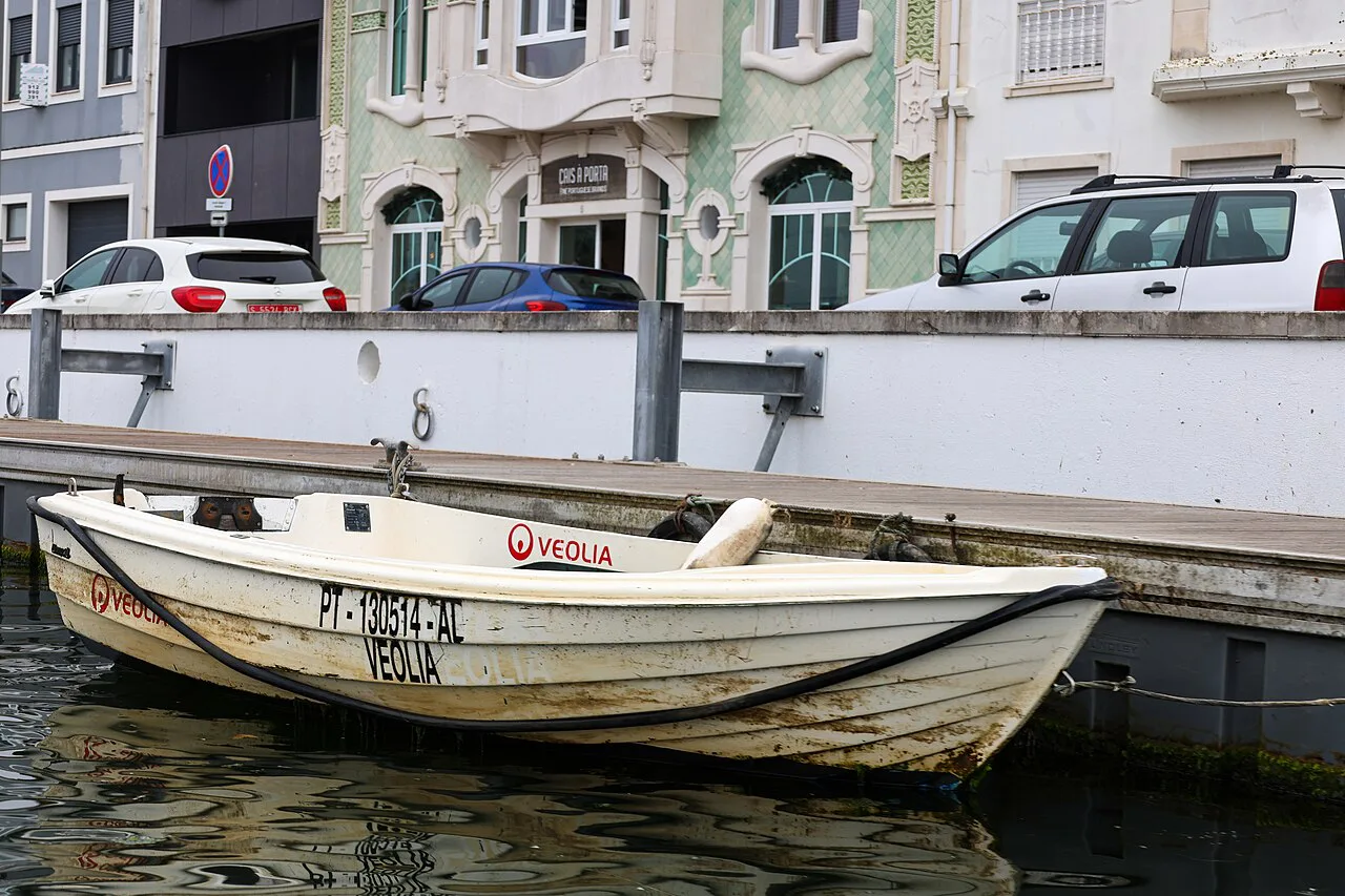 A small boat moored in a canal in Aveiro, with town buildings behind.