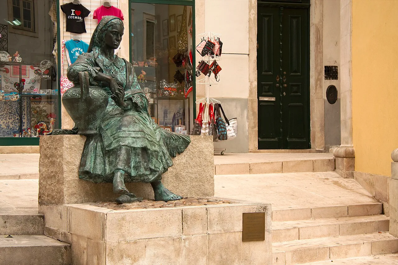 A bronze statue of a seated woman on a street in Coimbra's Baixa.