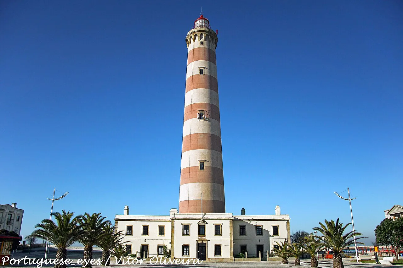 The striped Aveiro lighthouse rising above palms at Praia da Barra.