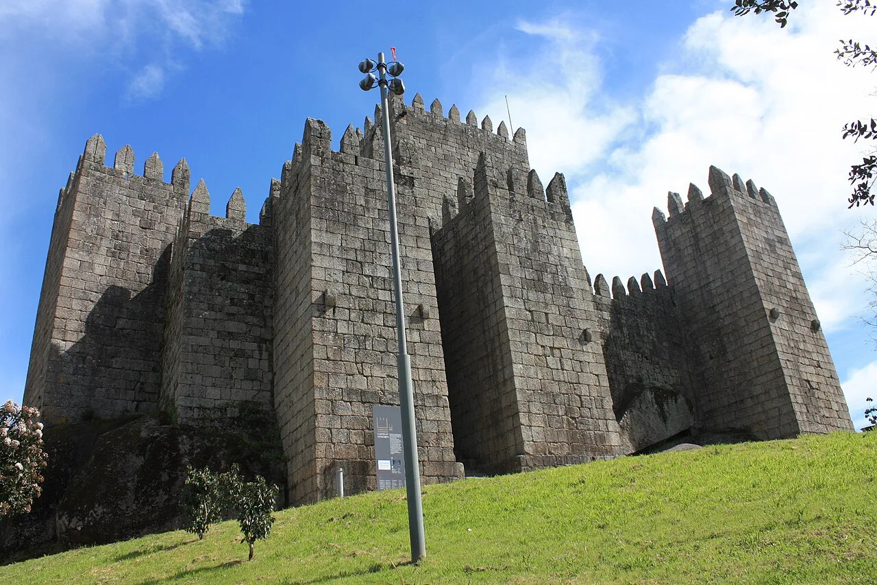 The towers and walls of Guimarães Castle above a grassy slope.