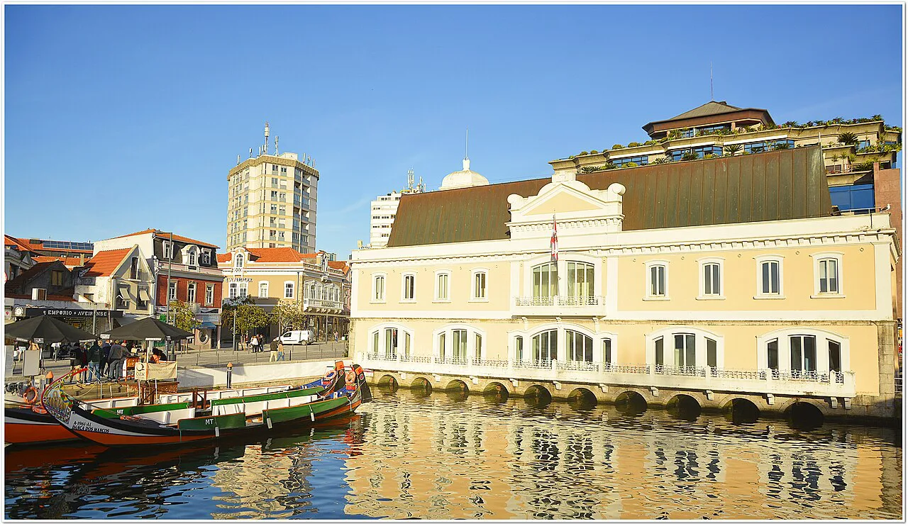 A moliceiro boat on a canal in Aveiro, in front of a pale yellow building.