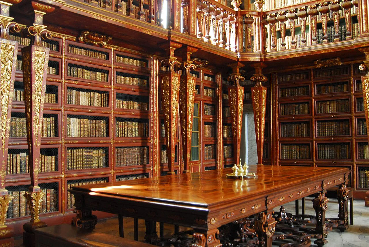 Gilded bookcases and a reading table inside the Biblioteca Joanina in Coimbra.
