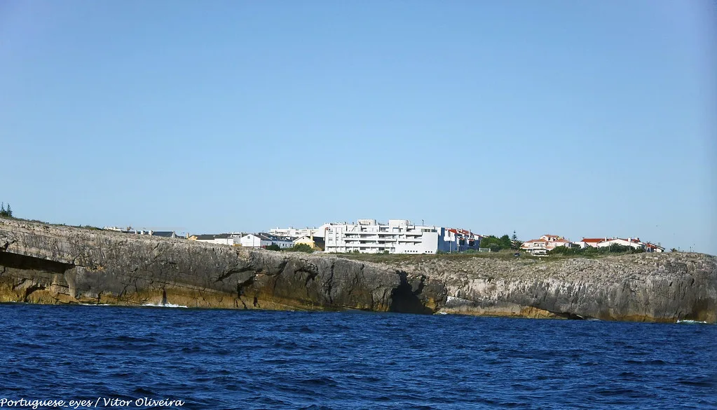 The rocky coastline of Peniche with buildings beyond the water.