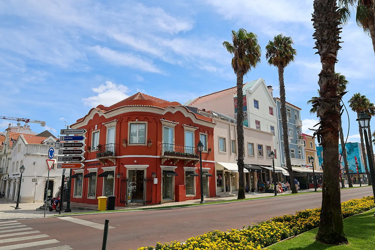 A red building and palm trees along a street in Cascais.