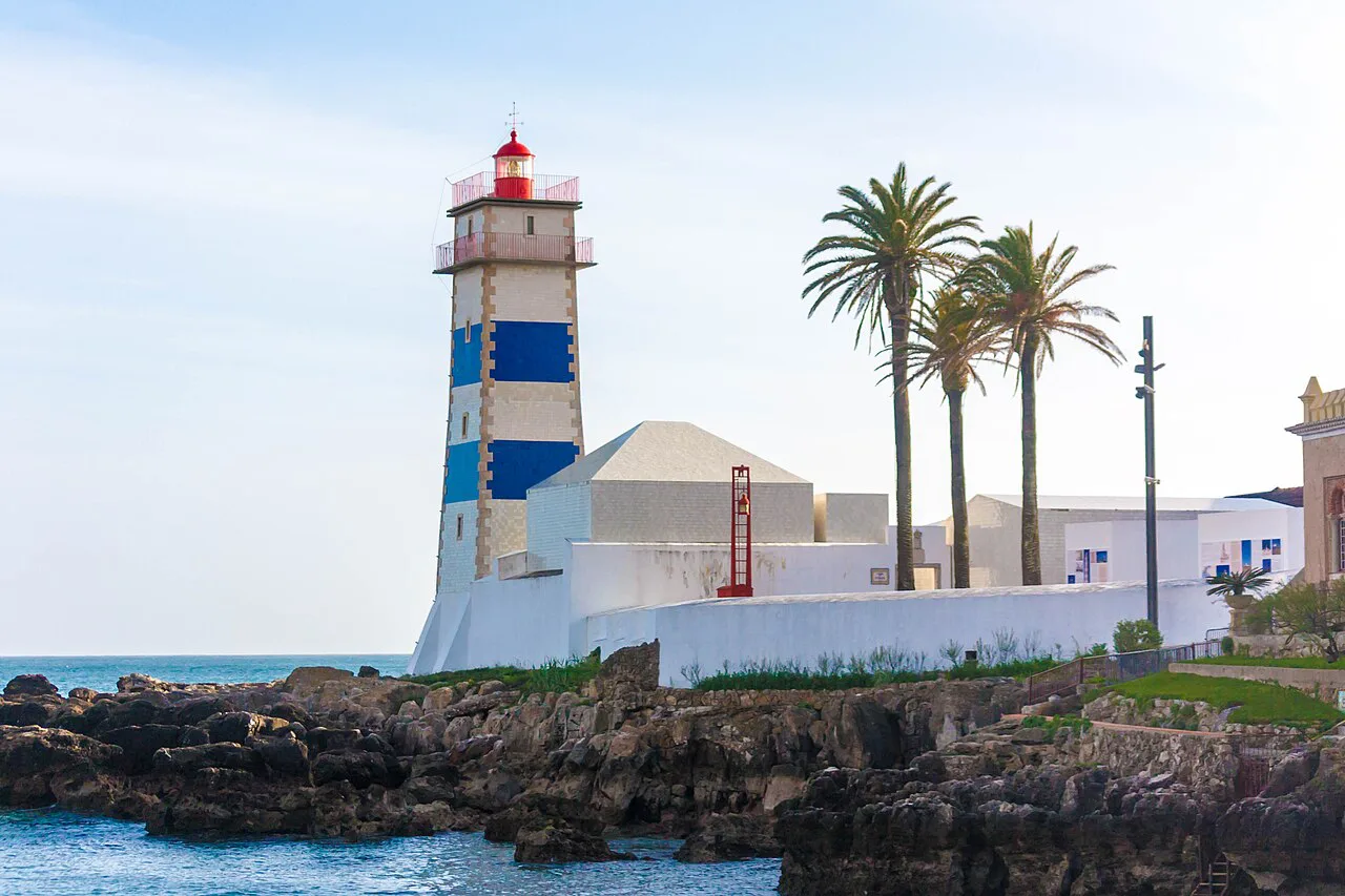 The blue-and-white striped Farol de Santa Marta on the rocky shore at Cascais.