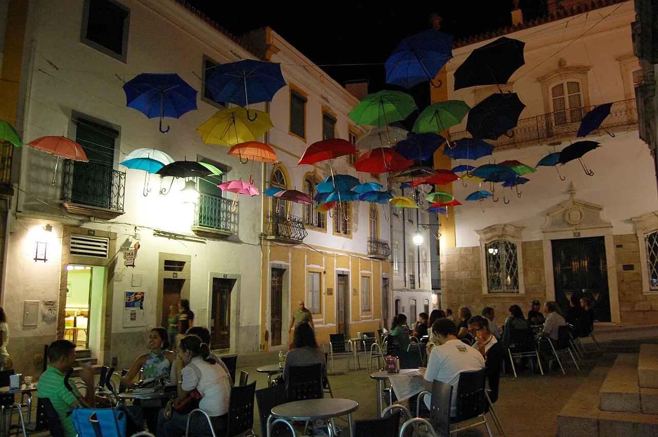 Café tables under hanging umbrellas at Largo de São Vicente in Évora's historic centre.