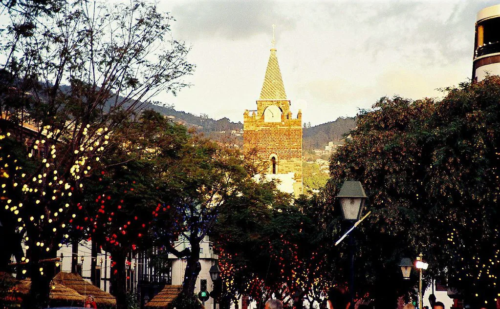 A church tower framed by trees strung with lights in Funchal.