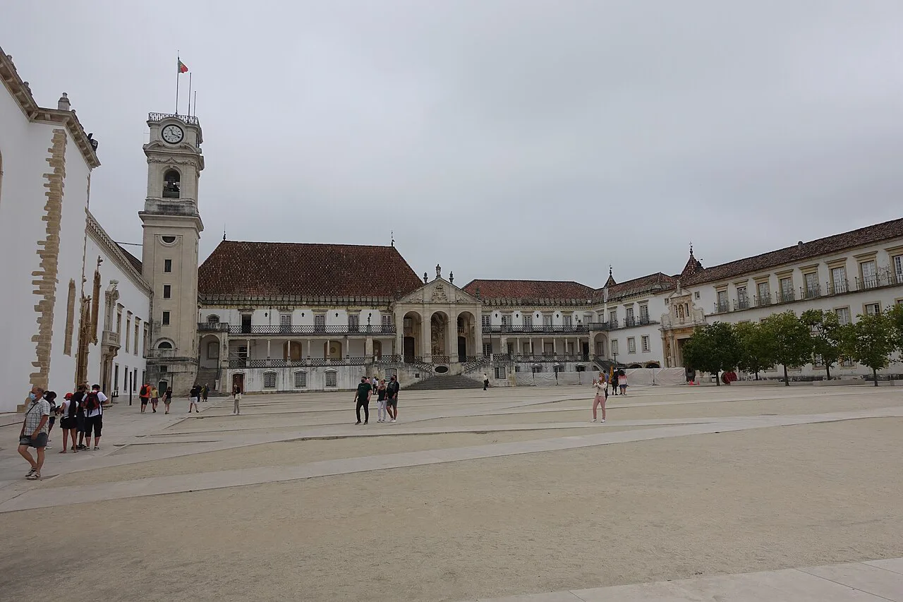 A paved courtyard framed by historic buildings and a clock tower in Coimbra.