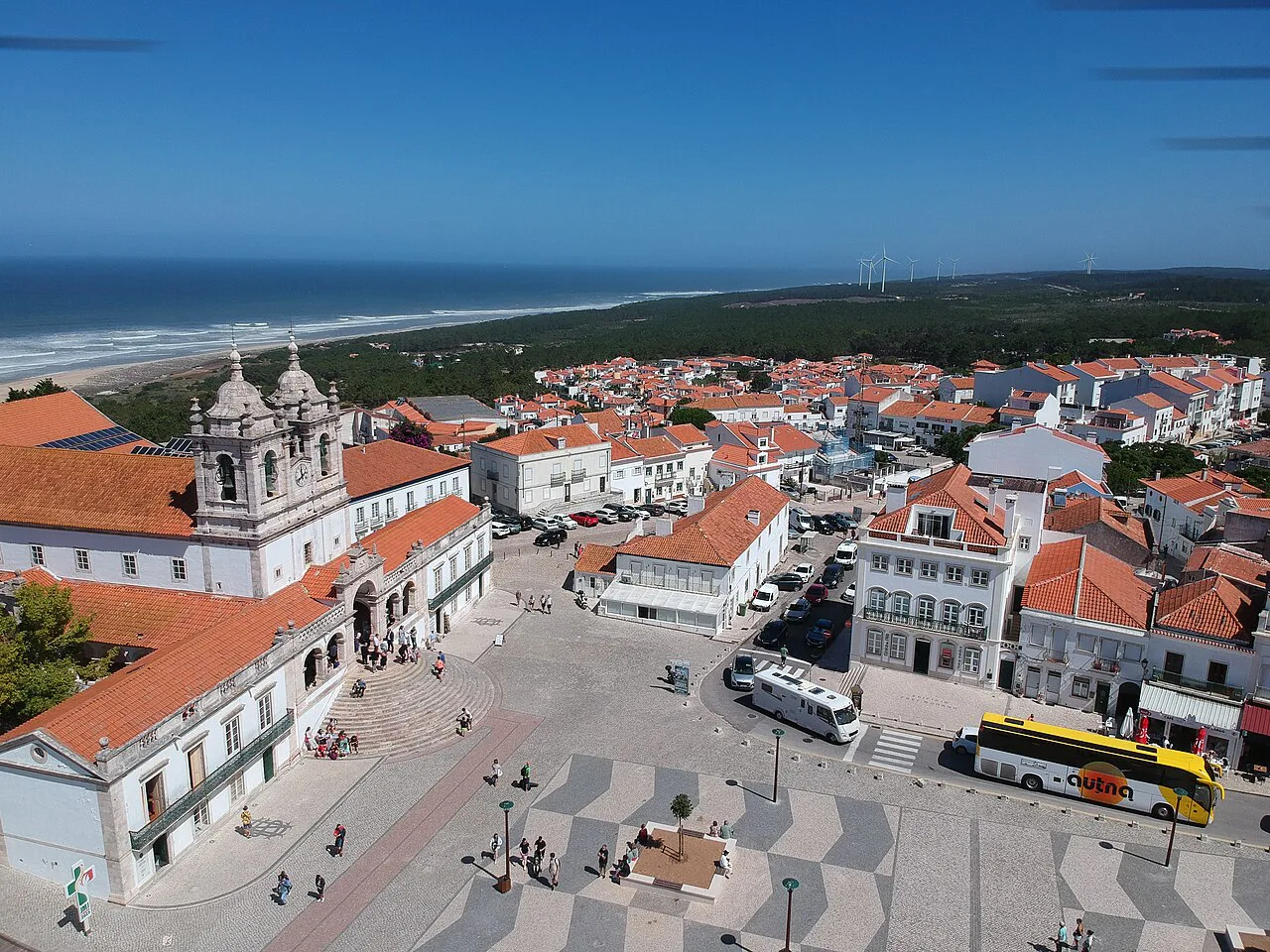 Aerial view over a square and rooftops in Nazaré towards the Atlantic.