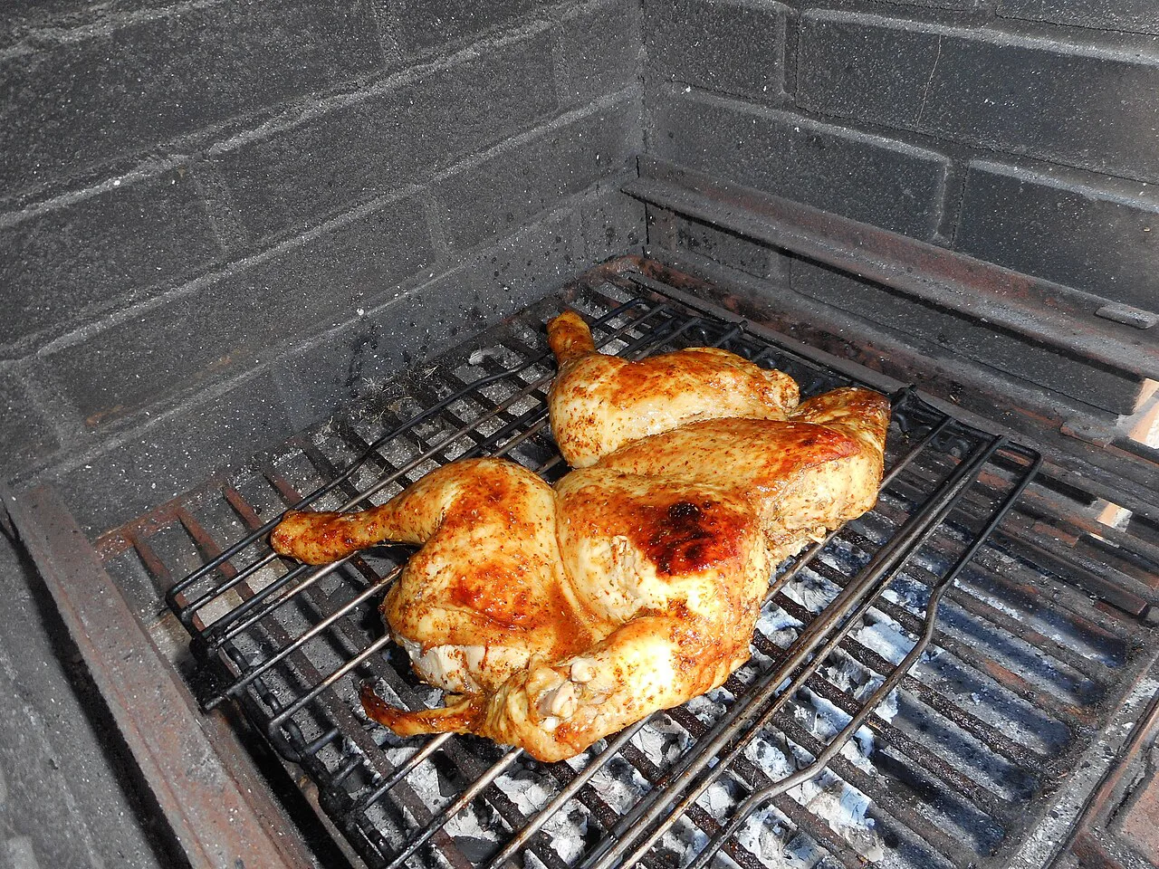 Piri piri chicken cooking on a charcoal grill.