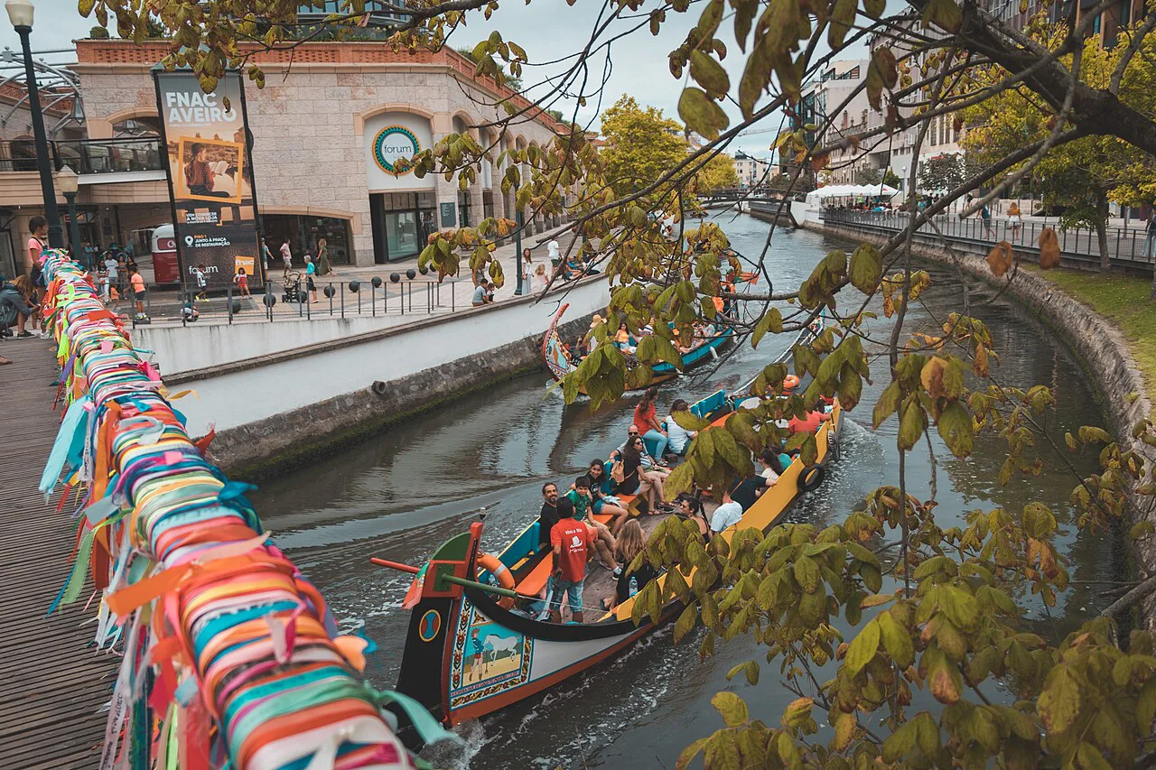 Coloured ribbons on a canal bridge railing above a moliceiro boat in Aveiro.