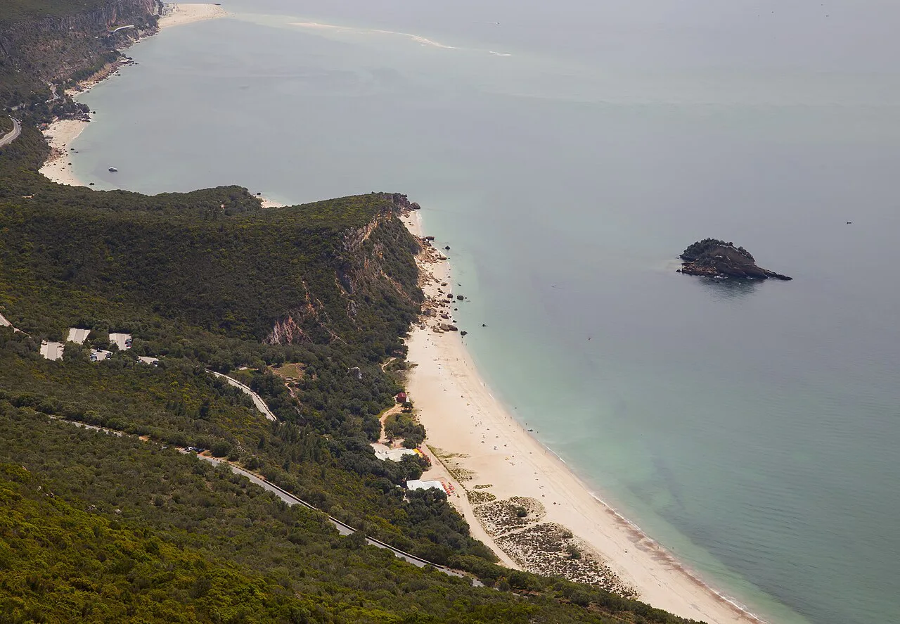 A sandy beach below the wooded slopes of the Arrábida Natural Park near Setúbal.