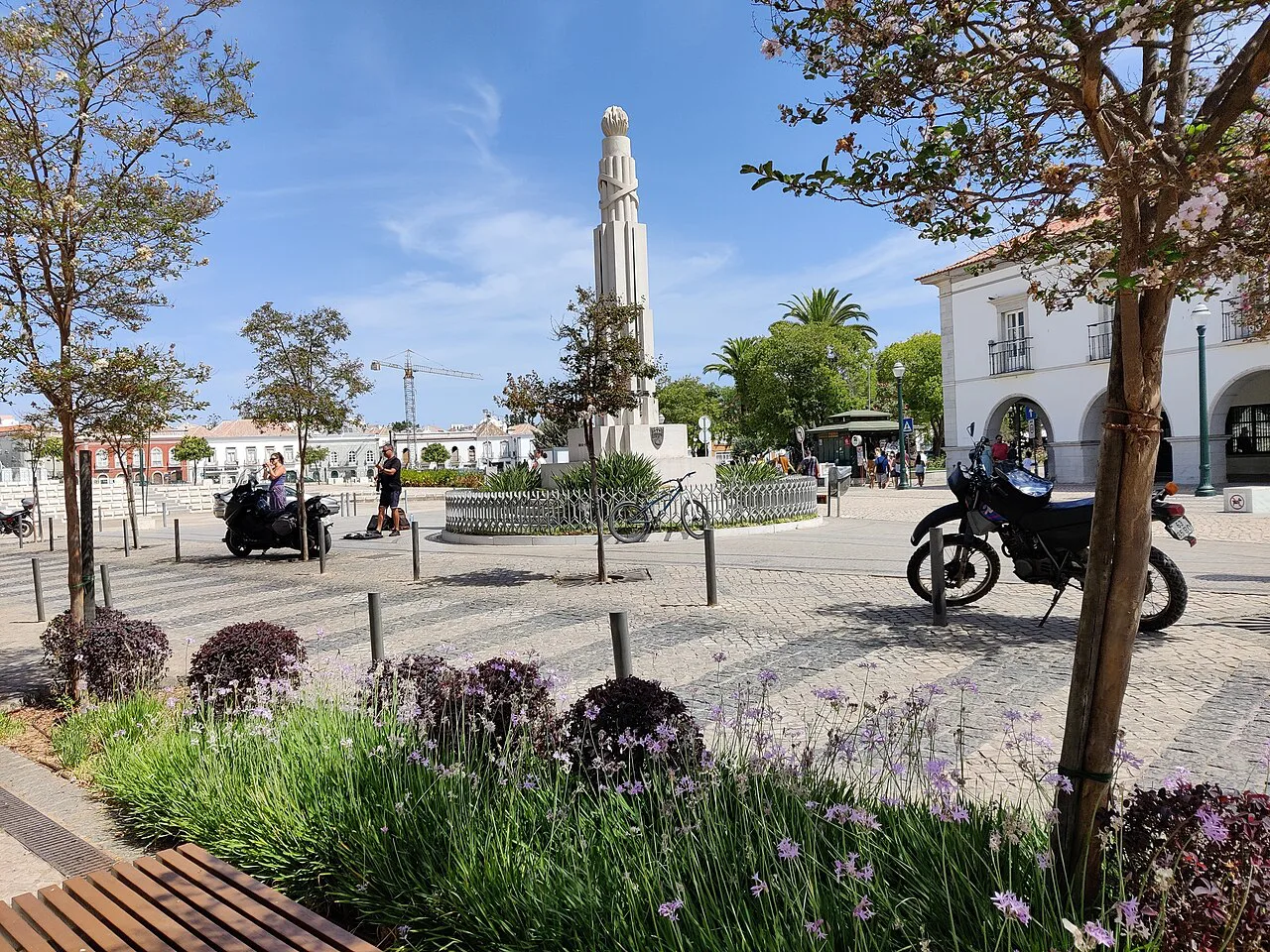 A square with a stone monument and trees in Tavira.