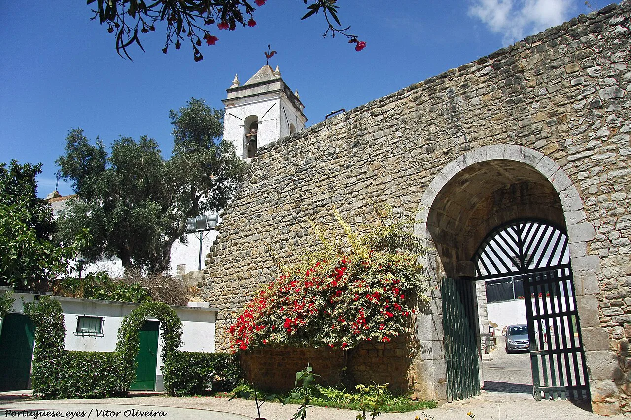 A gateway in the walls of Tavira Castle, framed by flowers.