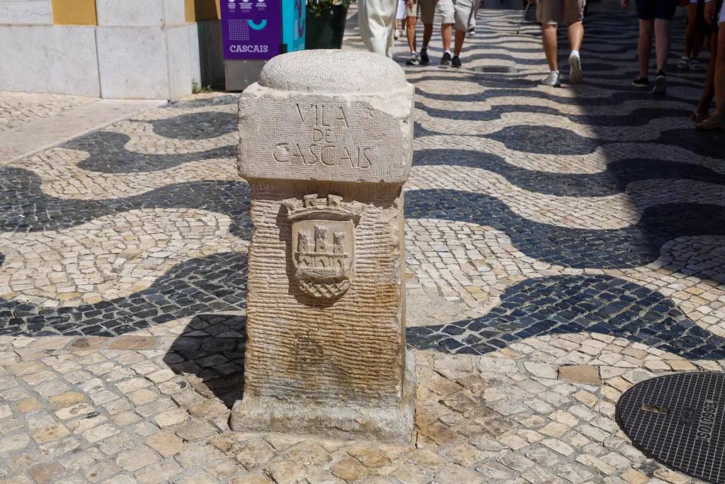 Wave-patterned cobbled pavement and a carved stone marker in Cascais.