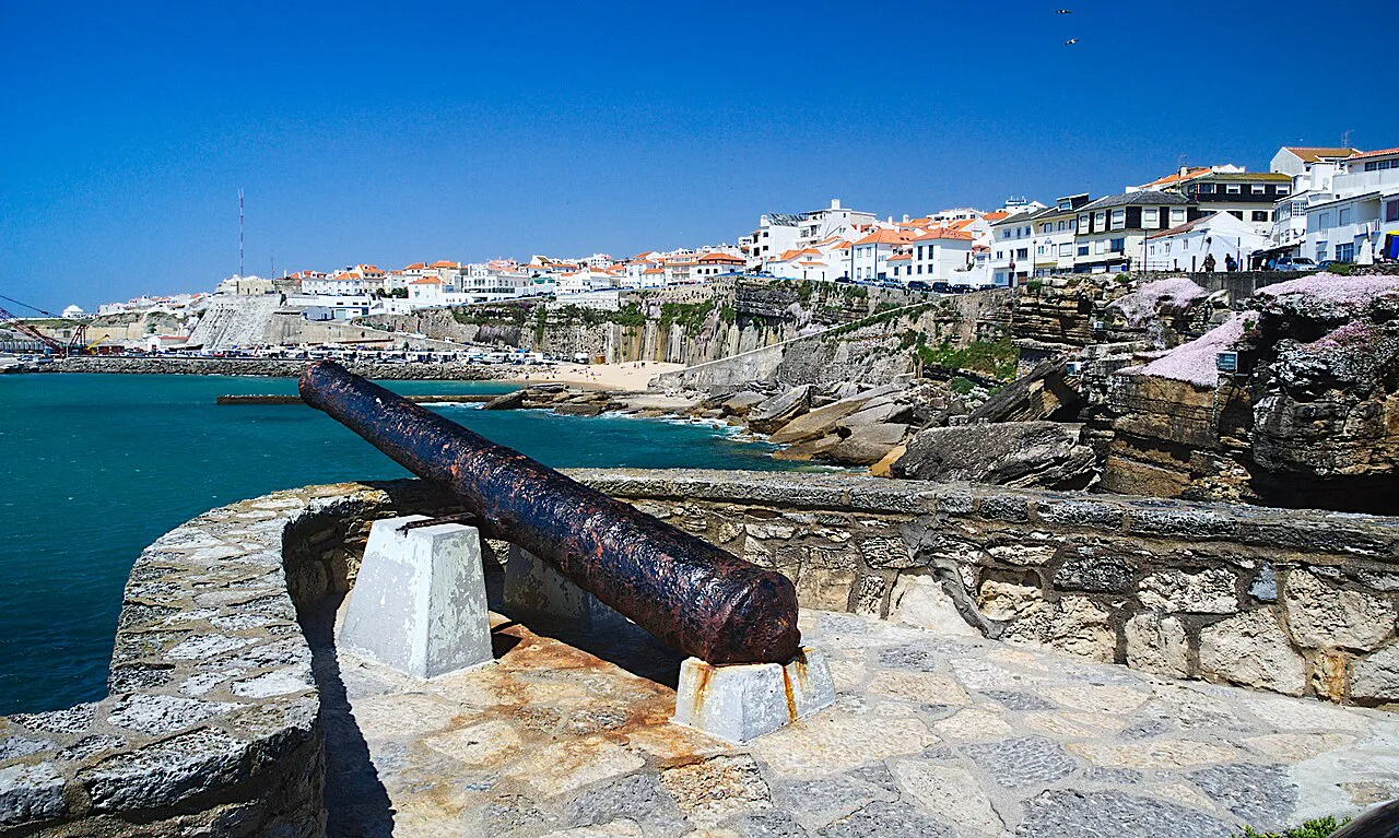 A view of Ericeira from the rocky seafront, with an old cannon in the foreground.